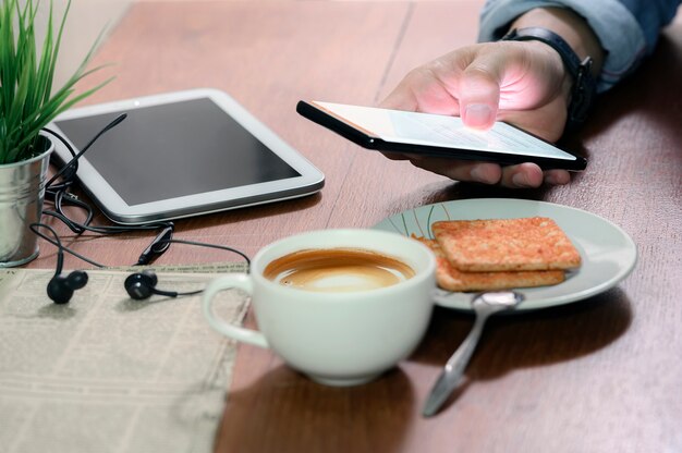 Tiro recortado da mão do homem usando o smartphone enquanto está sentado na mesa no café.