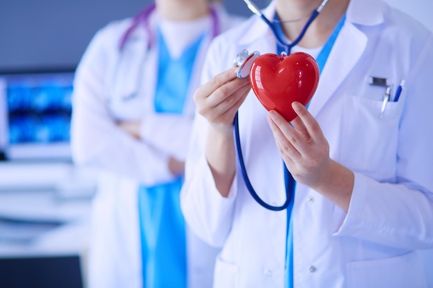 Tiro recortado de dois jovens médicos femininos com estetoscópio segurando coração