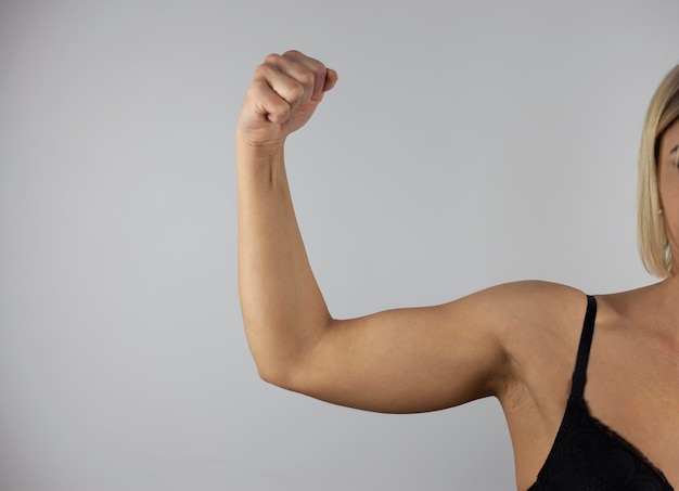 Foto tiro recortado de jovem mulher bronzeada em forma forte levantando o braço e mostrando o bíceps em um fundo branco feminismo poder feminino igual direitos das mulheres conceito de esportes de independência