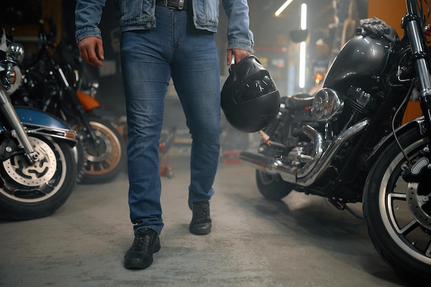 Tiro recortado de motociclista carregando capacete em pé sobre linha de motocicleta na garagem