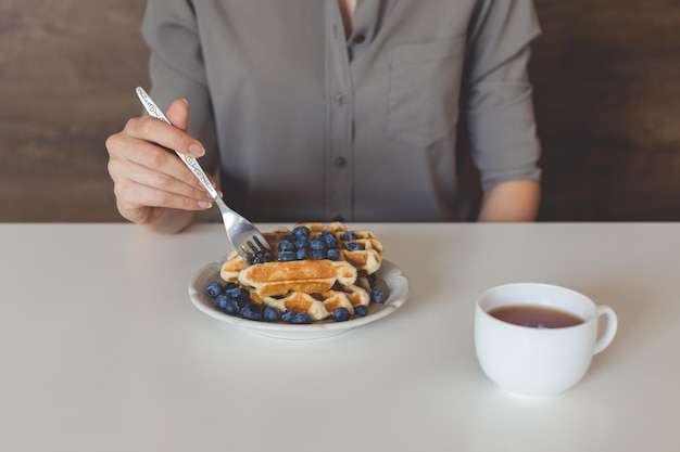 Tiro recortado de mulher comendo waffles com mirtilos no café da manhã