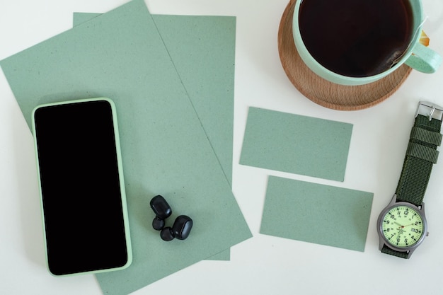 Tiro recortado de telefone inteligente de estilo masculino na mesa de escritório verde moderna com cartão de visita relógio de xícara de chá
