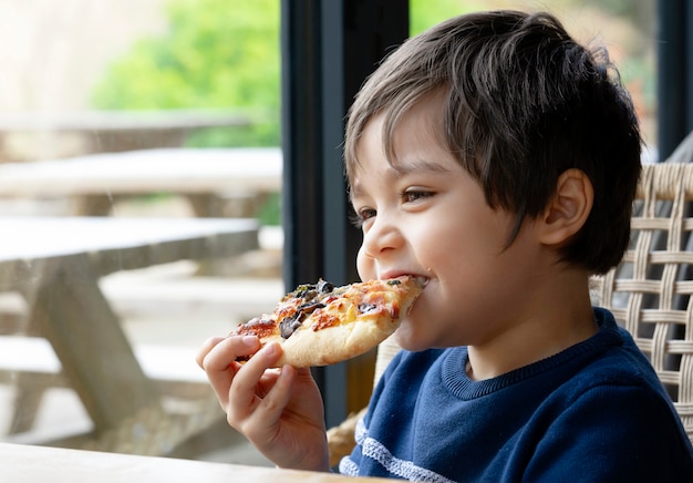 Tiro recortado garoto bonito garoto comendo pizza caseira no café