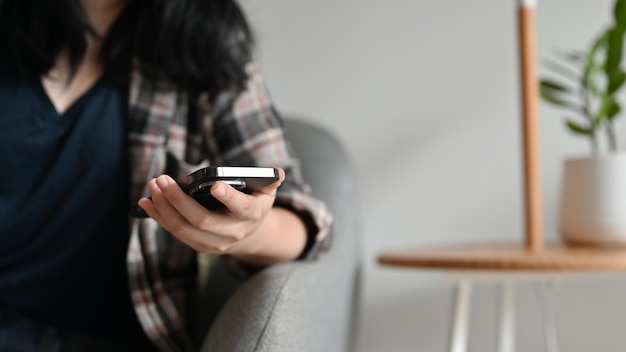 Tiro recortado Uma mulher asiática usando seu smartphone enquanto está sentado no sofá