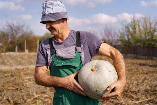 Foto tiro traseiro do agricultor autêntico homem sênior com abóbora no campo de milho