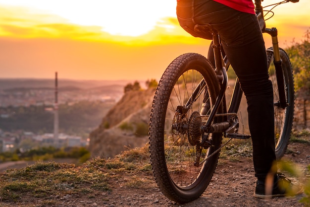 Foto tiro traseiro do motociclista da montanha ao pôr do sol, sentado em uma bicicleta