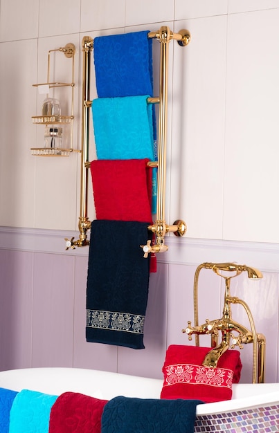 Un tiro vertical de coloridas toallas de bambú colgando de un estante dorado en un baño.