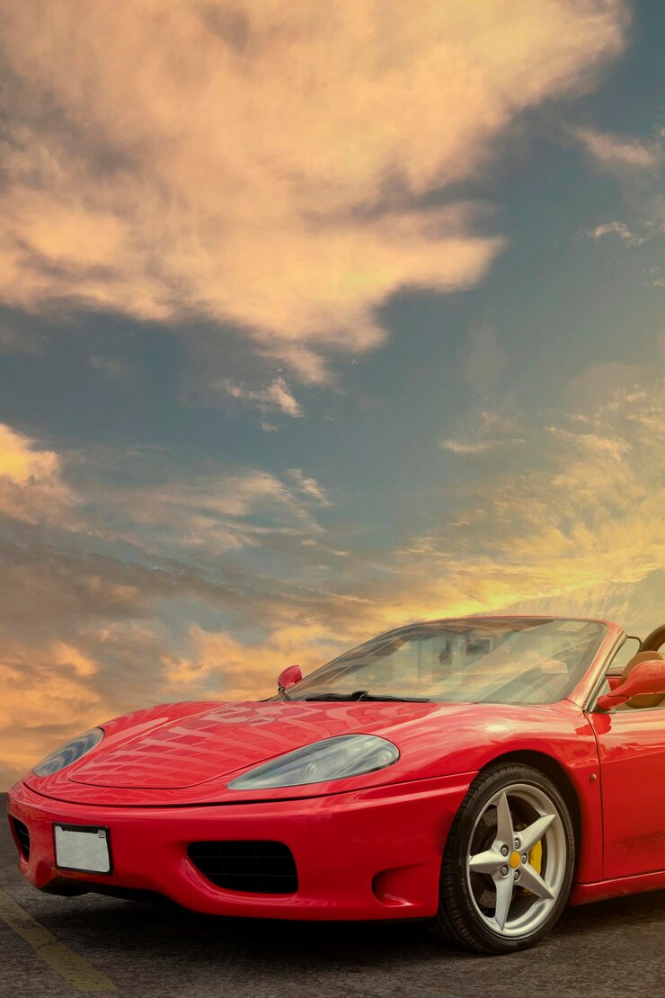Tiro vertical da frente de um carro esportivo vermelho com o pôr do sol ao fundo e espaço de cópia