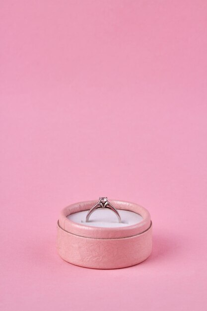 Tiro vertical de caixa de presente rosa com anel de noivado em fundo rosa