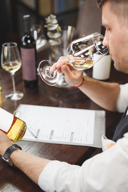 Foto tiro vertical de mordomo de vinho com forma cheira a bebida branca sentado à mesa