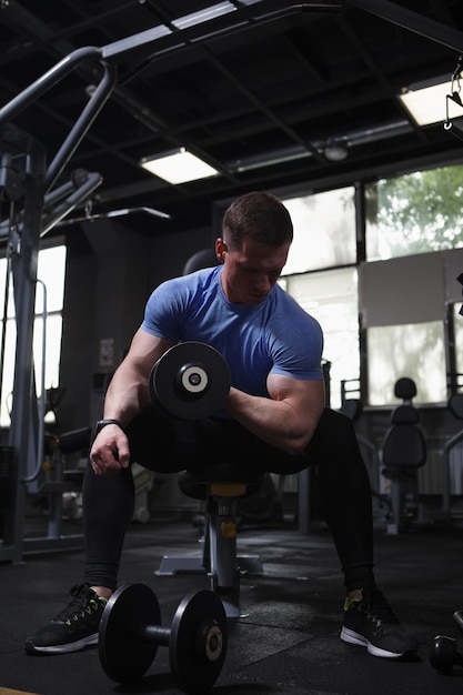 Tiro vertical de um homem atlético fazendo exercício de cachos de bíceps de halteres no ginásio