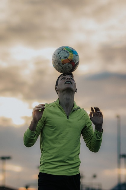 Foto tiro vertical de um jogador fazendo toques de cabeça e uma bola de futebol com o céu iluminado ao fundo