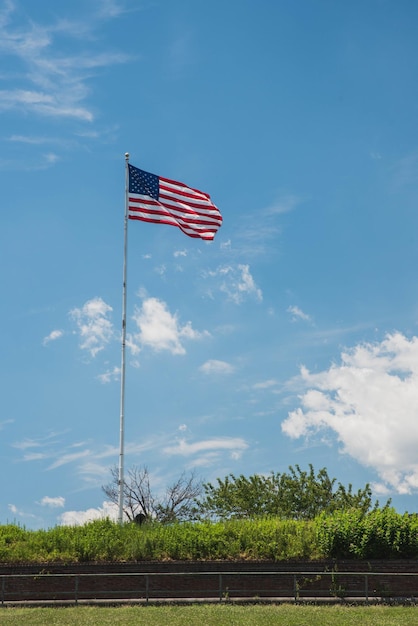 Tiro vertical de uma bandeira americana acenando em um poste com um fundo de céu azul