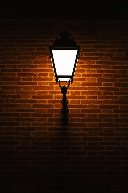 Foto tiro vertical de uma parede de tijolos com uma lâmpada de luz quente ao ar livre à noite
