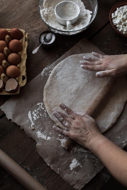 Tiro vertical de manos femeninas rodando masa con el tablero en la mesa de la cocina