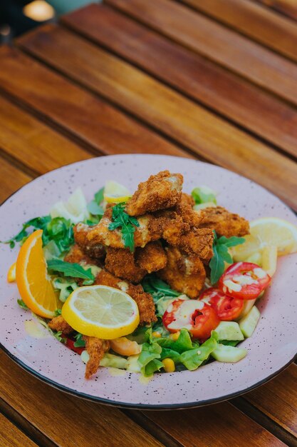 Tiro vertical de pollo frito en una deliciosa ensalada en un plato sobre la mesa en un restaurante