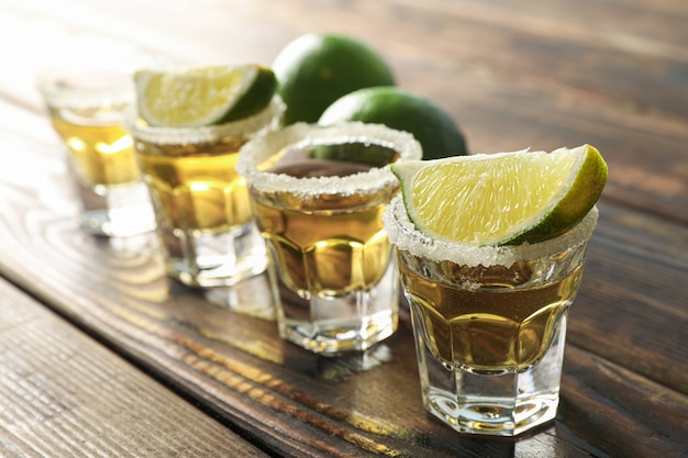 Tiros de tequila com fatias de sal e limão na mesa de madeira, closeup