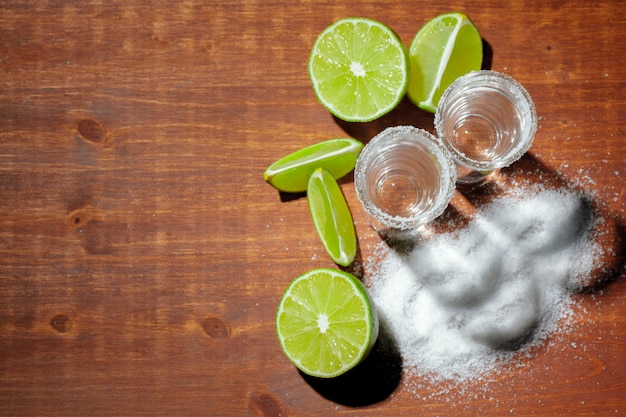 Tiros de tequila prata com fatias de limão e sal na placa de madeira