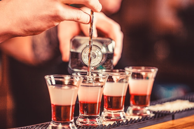 Tiros na boate. Bebida alcoólica vermelha em copos no bar. Coquetel vermelho na boate. Barman preparando o atirador de coquetéis.