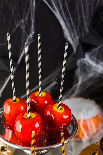 Tisch mit farbigen Süßigkeitsäpfeln und Kuchen für Halloween-Party.