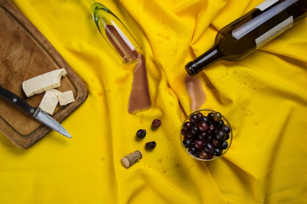 Tisch mit gelber Tischdecke mit Glas und Flasche Wein, begleitet von Trauben und Käse