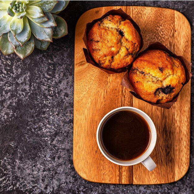 Tisch mit Muffins, Blumen und Kaffee.