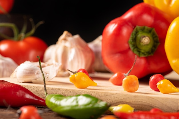 Tisch mit roten und gelben Paprikaschoten, Zwiebeln und Knoblauch und Tomaten über rustikalem Holz, schwarzem Hintergrund, selektiver Fokus