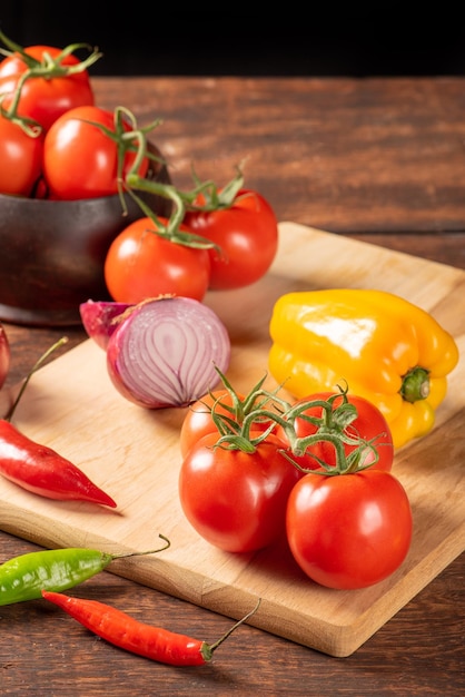 Tisch mit roten und gelben Paprikaschoten, Zwiebeln und Knoblauch und Tomaten über rustikalem Holz, schwarzem Hintergrund, selektiver Fokus