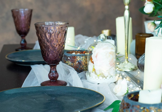 Tisch serviert mit burgunderroten Gläsern Blumenkerzen und Girlande Ein Glas mit Teller Kerzen