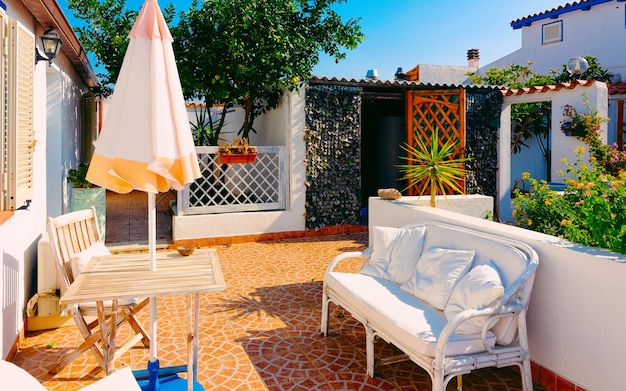 Tisch und Sofa auf der Veranda des Cafés oder Restaurants im Luxusresort Costa Smeralda auf der Insel Sardinien in Italien im Sommer. Gemütliche Veranda mit Stuhl und Sonnenschirm in der sardischen Stadt in Sardinien. Gemischte Medien.