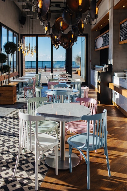 Tisch und Stühle in einem stilvollen Café-Interieur im Vintage-Stil, mit großen Fenstern und Meerblick