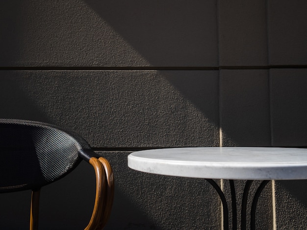 Tisch und Stuhl gegen graue Wand im Café. Sonnenlicht trifft auf einen leeren Kaffeetisch