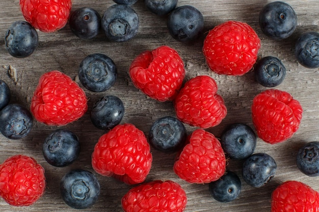 Tischansicht - Nahaufnahme von Heidelbeeren und Himbeeren, verschüttet auf grauem Holzschreibtisch.