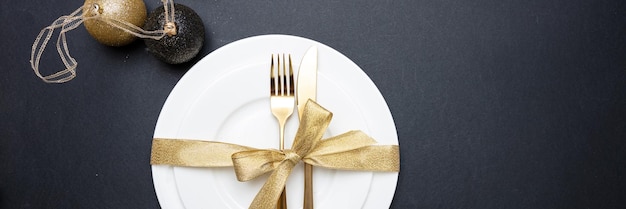 Tischdekoration Weihnachten Neujahr Goldbesteck auf weißem Geschirr schwarzer Hintergrund