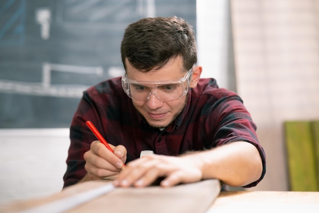 Tischler bei der Arbeit Mann misst und markiert Holzbrett mit Metalllineal und Bleistift