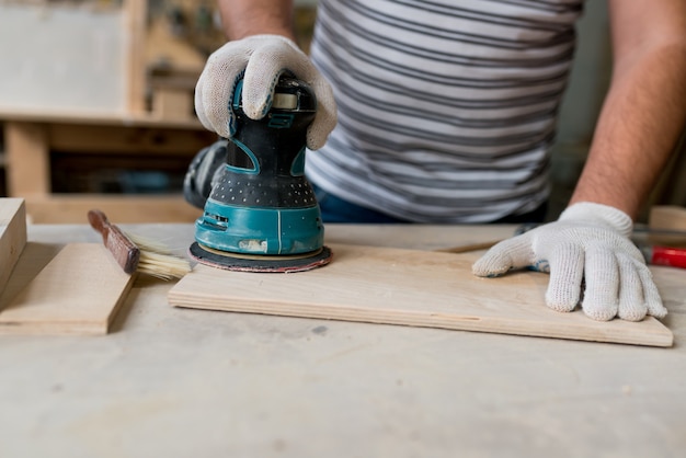 Tischler, der mit Holz arbeitet, mit elektrischem Schleifer aus der Werkstatt