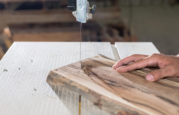 Tischlerhände, die an einer Bandsäge mit Holzform arbeiten, um Innenprodukte herzustellen