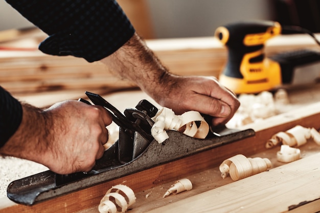 Tischlerhände, die eine Holzplanke mit einem Handhobel hobeln