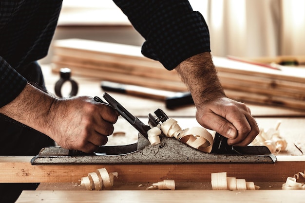 Tischlerhände, die eine Holzplanke mit einem Handhobel hobeln