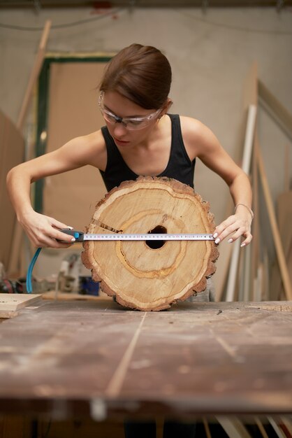 Tischlerin mit Maßband und Sägeschnittbaum in den Händen in der Werkstatt