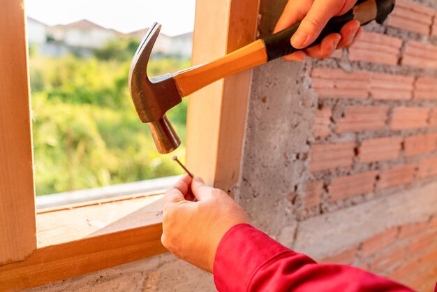 Tischlermann, der mit dem Hämmern eines Nagels in einen Holzfensterrahmen-Konzeptbau arbeitet, der auf der Baustelle arbeitet