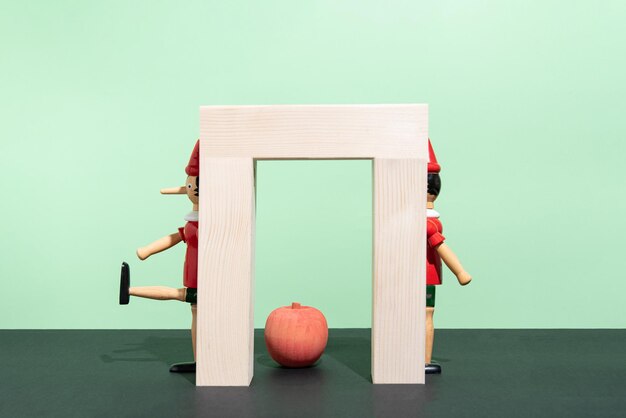 Foto títere de madera detrás de una puerta de madera y una manzana sobre un fondo verde y negro