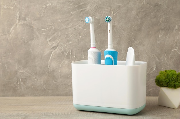 Titular con cepillos de dientes eléctricos modernos y planta sobre fondo gris