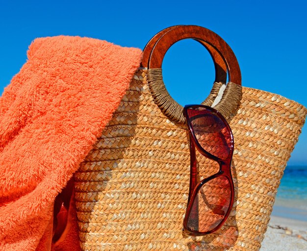 Toalha de óculos de sol e bolsa de palha por uma praia tropical