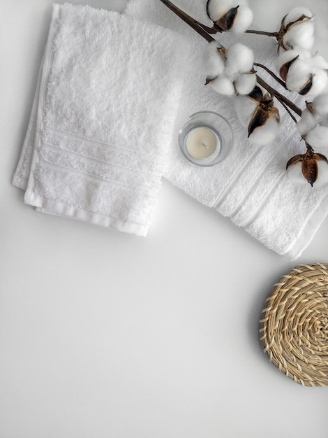 Toalhas brancas com ramo de flores de algodão e vela de cera no fundo branco