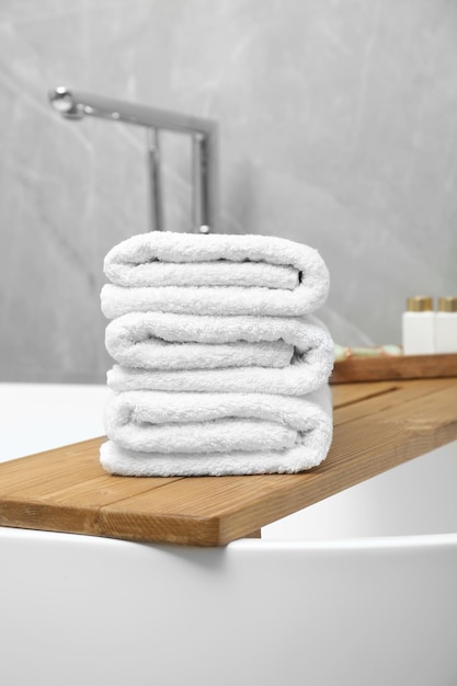 Toalhas de banho empilhadas e produtos de higiene pessoal na bandeja da banheira no banheiro