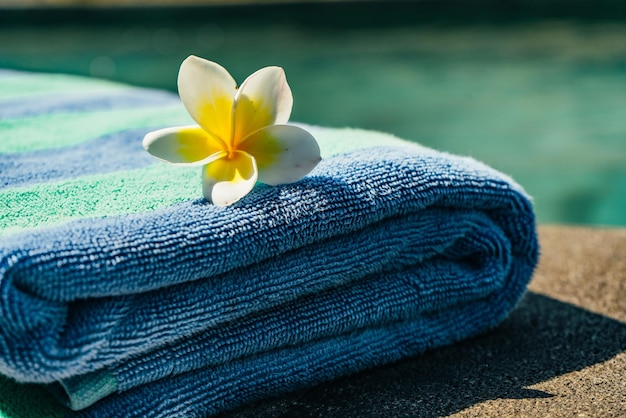 Toalla azul y flor franjipani cerca de la piscina