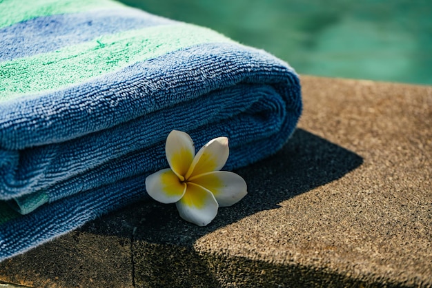 Toalla azul y flor franjipani cerca de la piscina