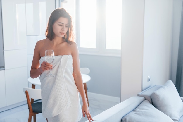 En una toalla blanca, la mujer joven está adentro en la habitación de una casa moderna durante el día