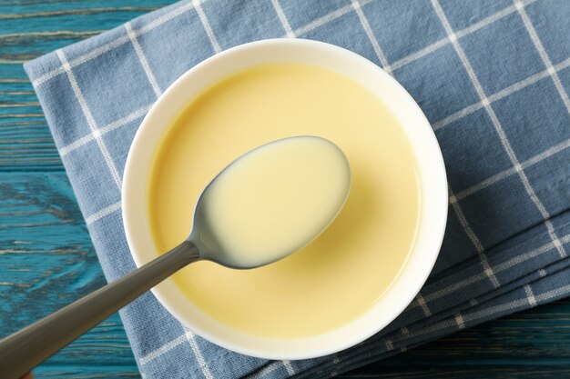 Toalla, cuchara y recipiente con leche condensada sobre fondo de madera